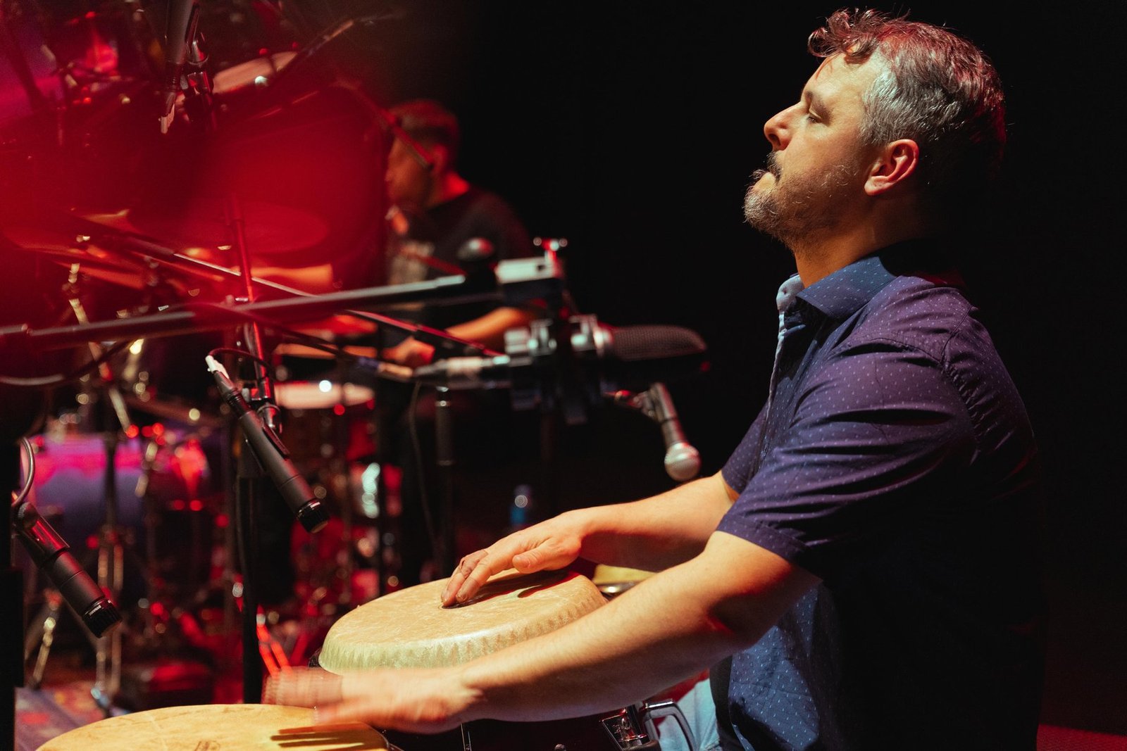 Odei Lizaso percusionista profesional tocando congas en concierto con luz roja
